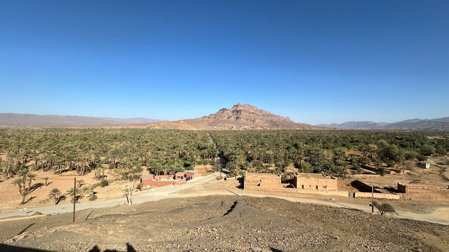 Wide view of the Draa Valley palm oasis near Agdz with mud-brick kasbahs and the Kissane mountain behind