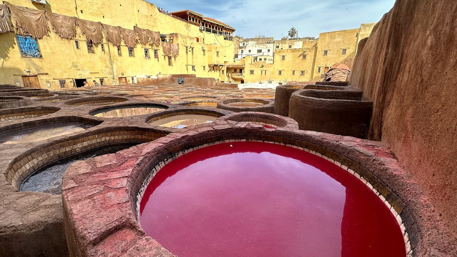 Close-up of a stone vat of deep red dye at the Chouara Tannery in Fes, with more dye pits and the medina rooftops behind