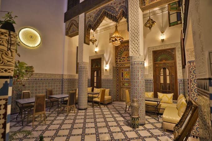 Ornate courtyard of a traditional riad in Fes with zellige tile floor, carved stucco arches and lanterns